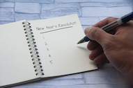 Caucasian hand and holding pen to pad that says "New Year's Resolution, 1., 2., 3., 4., 5."